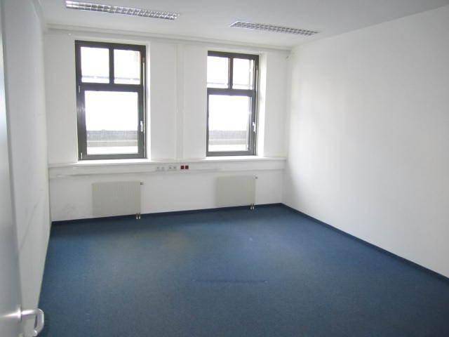 Kleiner, leerer Büroraum mit blauem Teppichboden, weißen Wänden und zwei großen Fenstern.