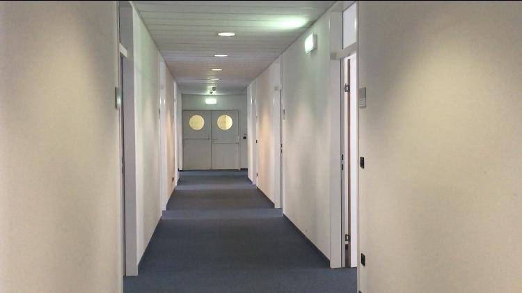 Langer, heller Flur mit Teppichboden, weißen Wänden und mehreren Türen, der zu weiteren Räumen führt.