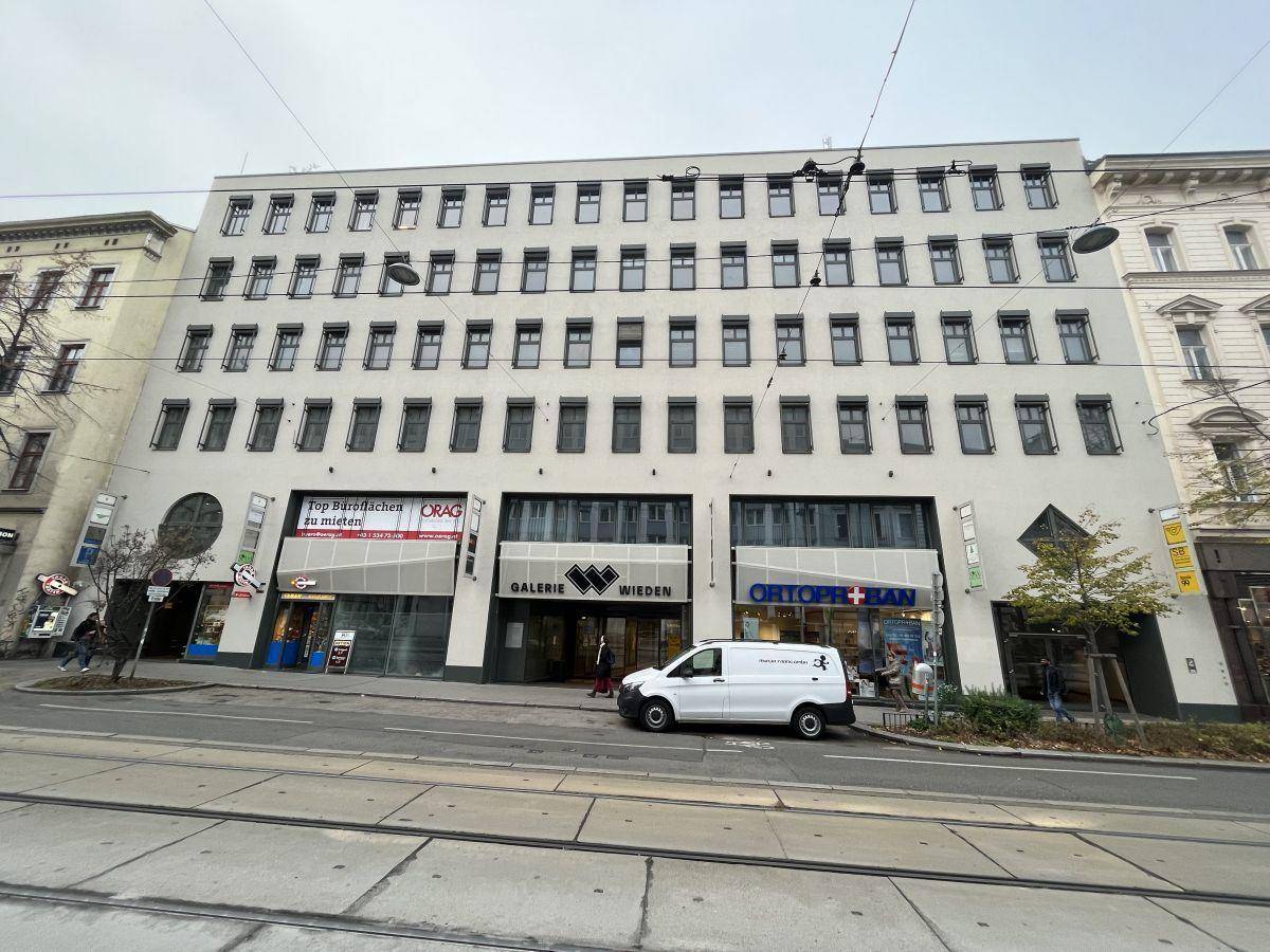 Mehrstöckiges Geschäftsgebäude an einer belebten Straße mit Geschäften im Erdgeschoss und vielen Fenstern.