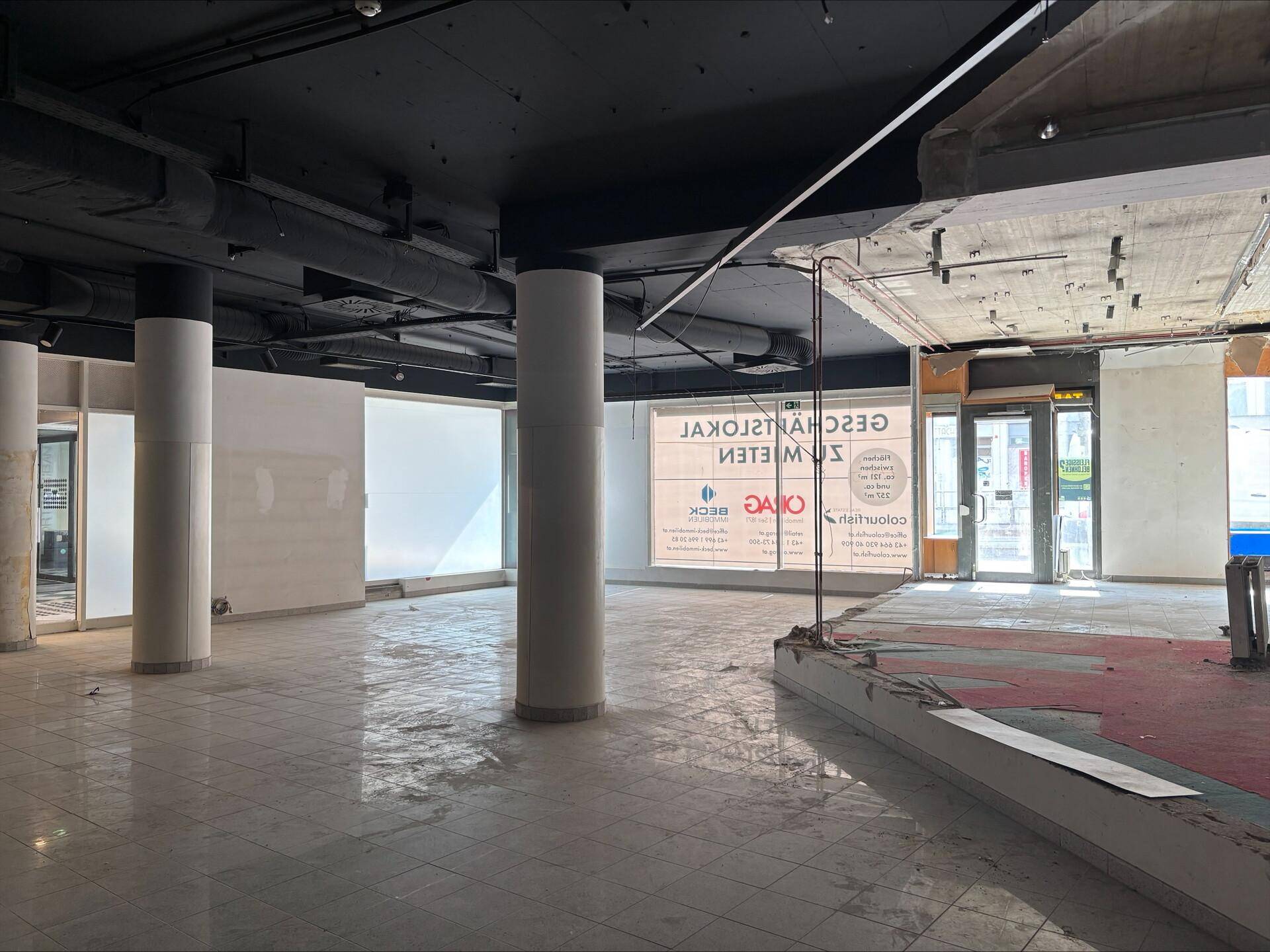 Geräumiges Ladenlokal mit Säulen, Fliesenboden und Blick durch die Schaufenster auf die Straße.