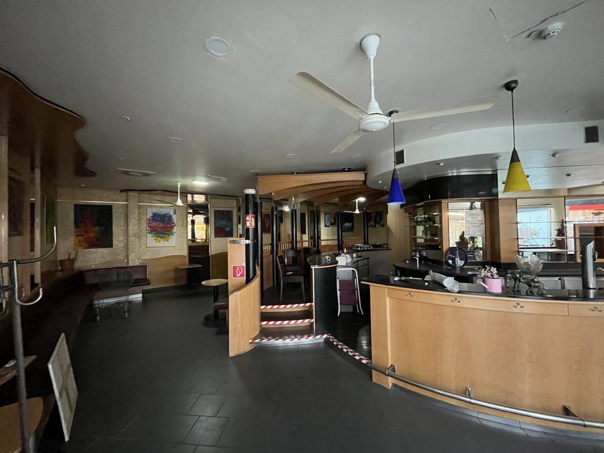 Innenansicht einer Bar mit Holzverkleidung, Deckenventilatoren und bunten Hängelampen über der Theke.
