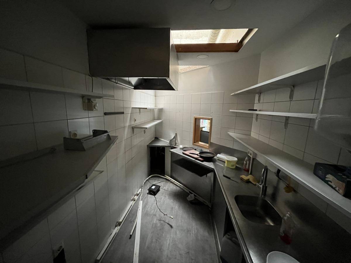 Professionelle Küche mit Edelstahl-Arbeitsflächen, Fliesenwänden und Abluftsystem unter einem Dachfenster.
