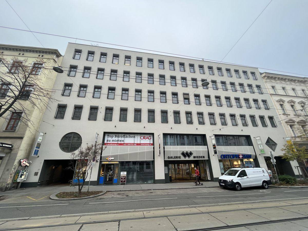 Modernes Geschäftsgebäude mit mehreren Etagen, großen Fenstern und Ladenflächen im Erdgeschoss.