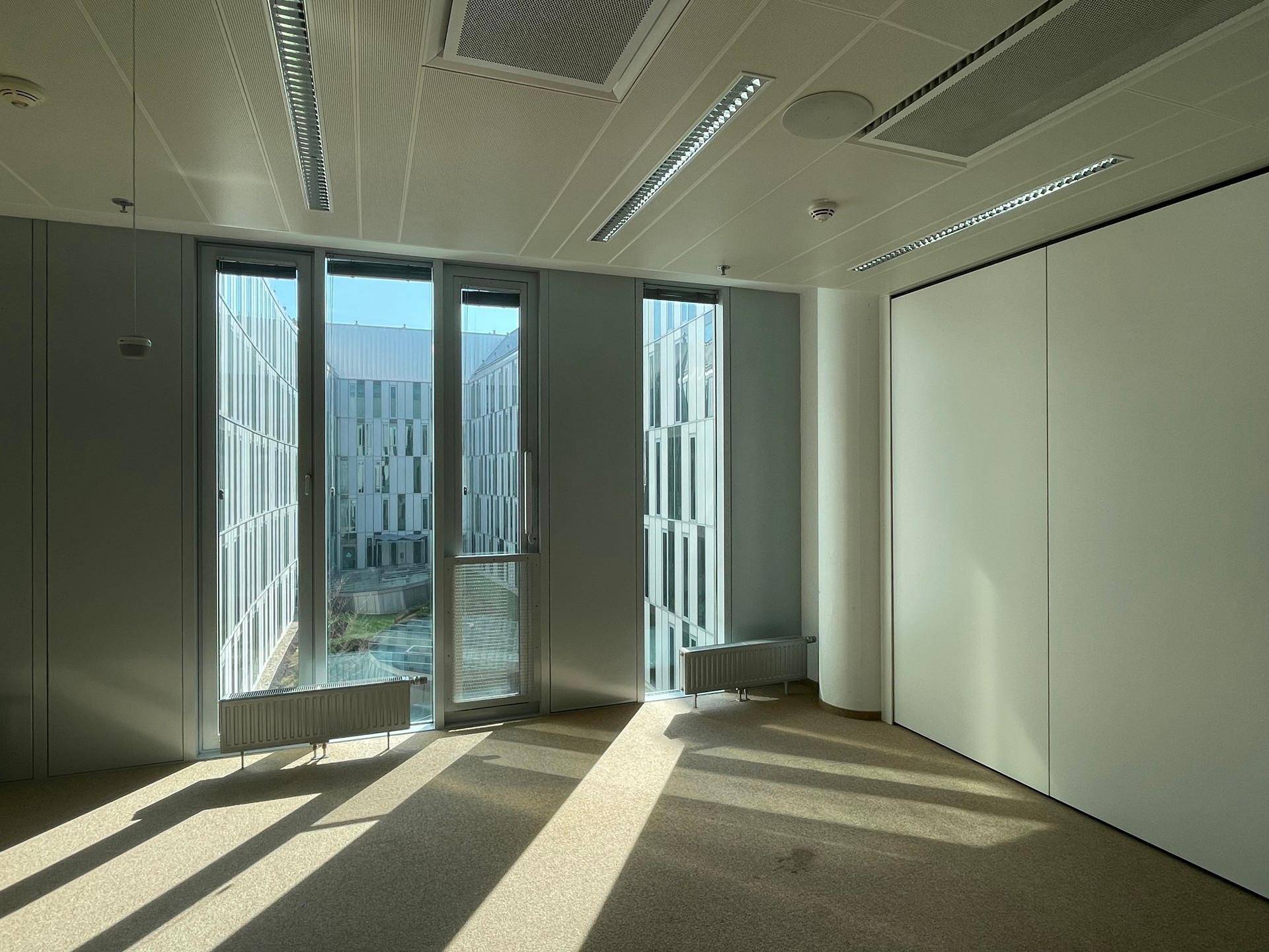 Leeres Büro mit Teppichboden und Fenstern, die auf einen Innenhof blicken.