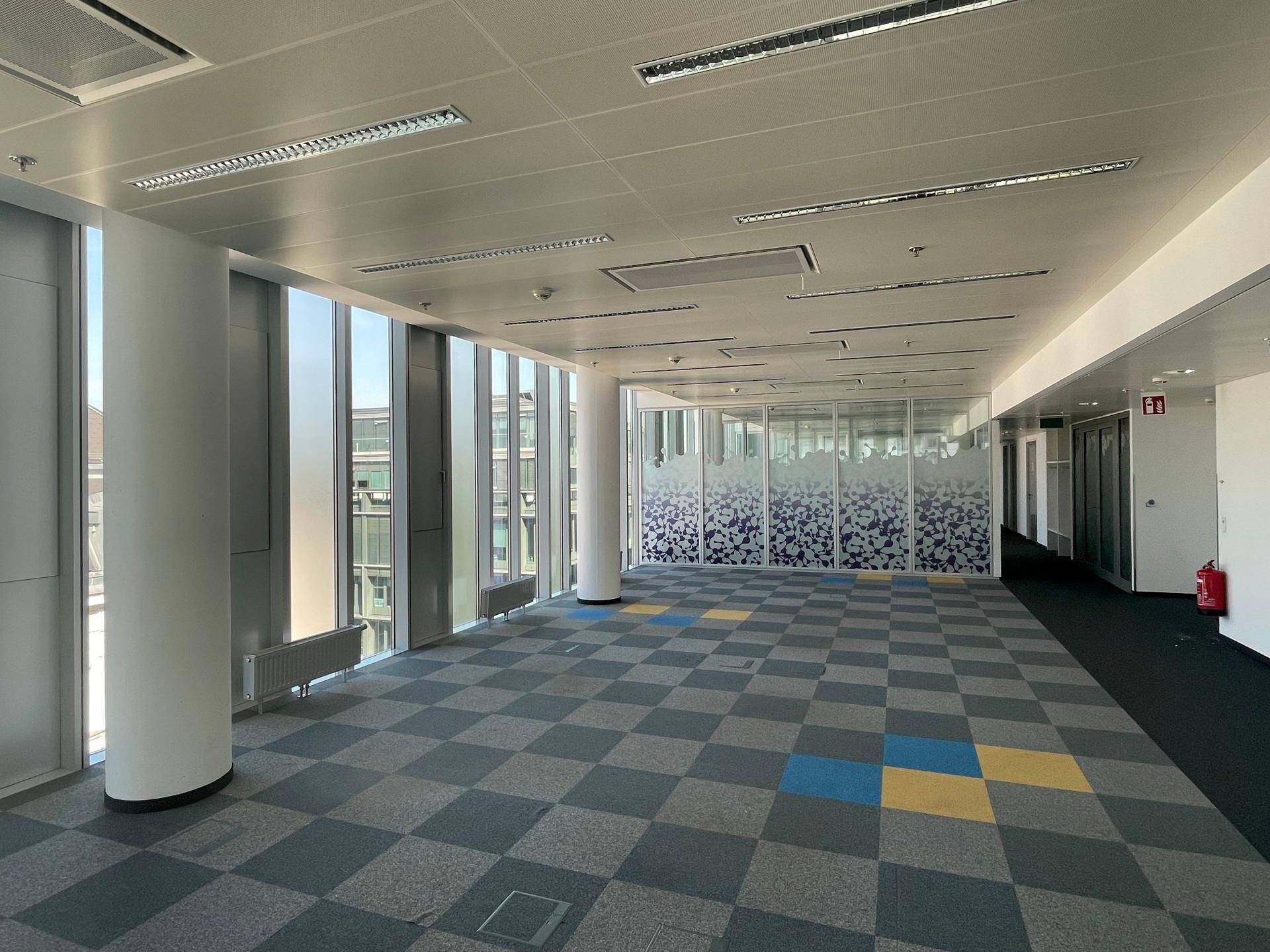 Großes, offenes Büro mit kariertem Teppichboden und modernen Glaswänden im Hintergrund.