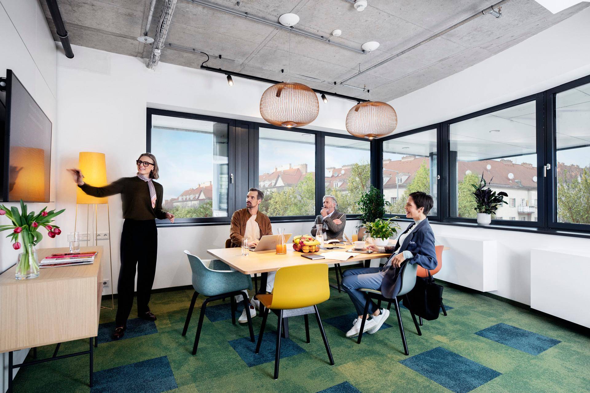 Moderner Konferenzraum mit bunten Stühlen, großem Fenster und Blick ins Grüne, ideal für Besprechungen.