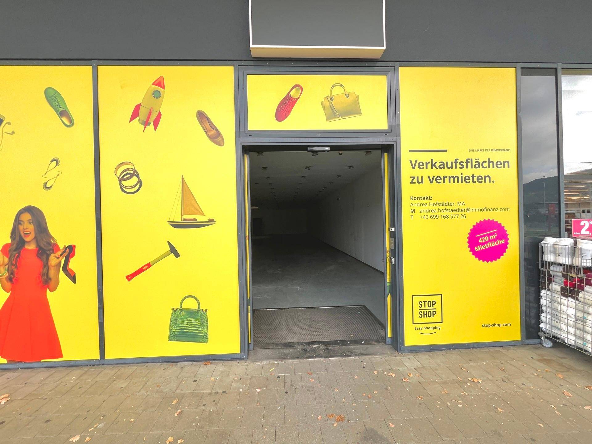 Eingangsbereich einer Gewerbefläche mit großen gelben Schaufenstern und Vermietungsanzeige, einladend gestaltet.
