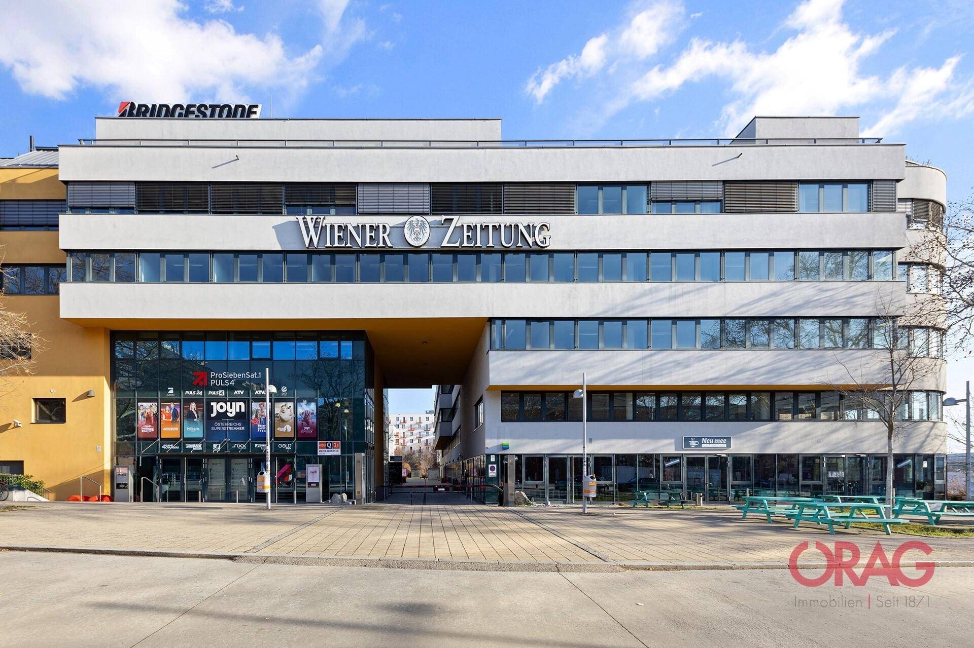 Modernes Geschäftsgebäude mit mehreren Etagen, großen Fenstern und kommerziellen Mietflächen im Erdgeschoss.