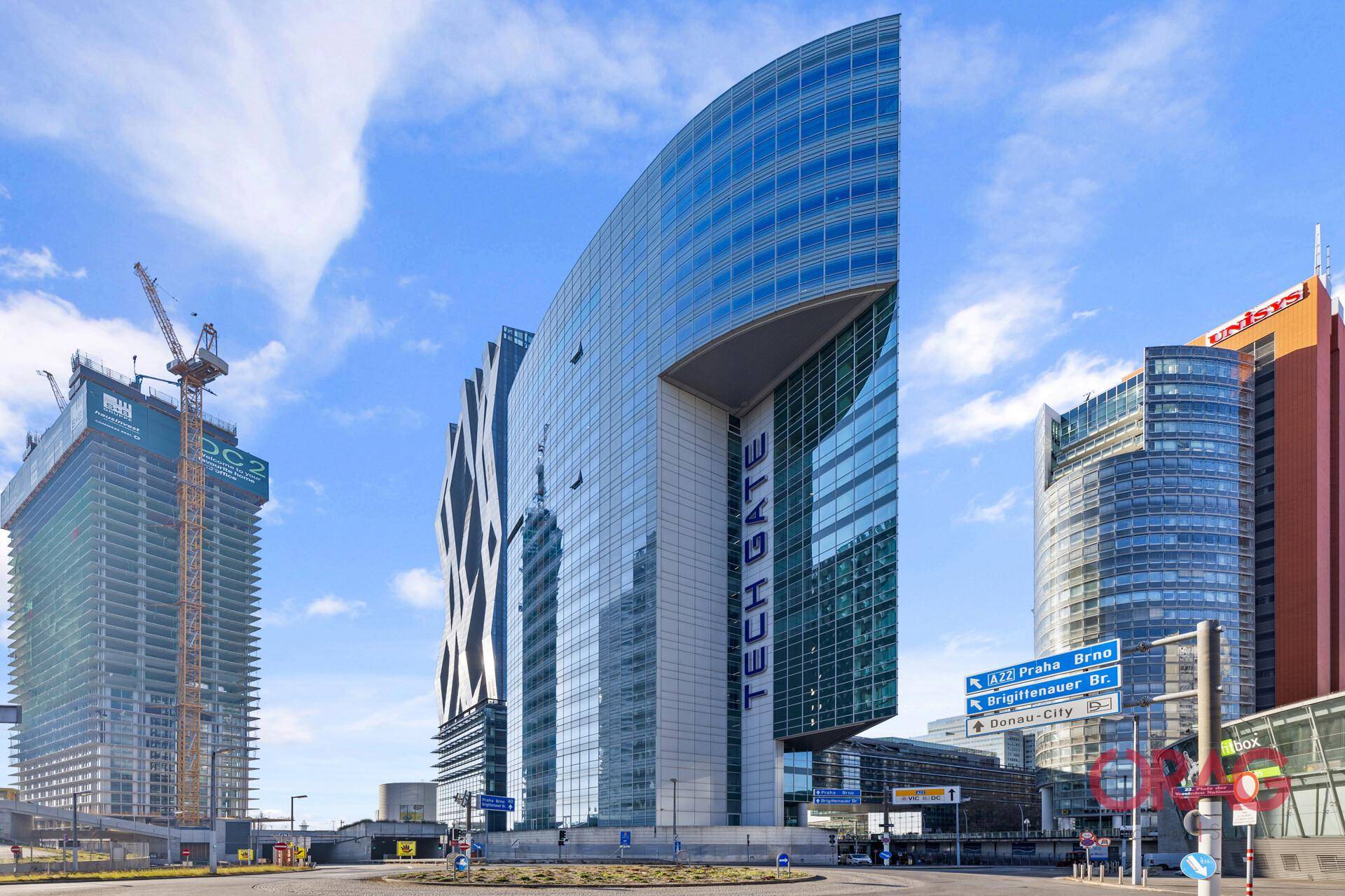 Moderne Glasfassade des Tech Gate Gebäudes mit weiteren Hochhäusern und einer Baustelle im Hintergrund.