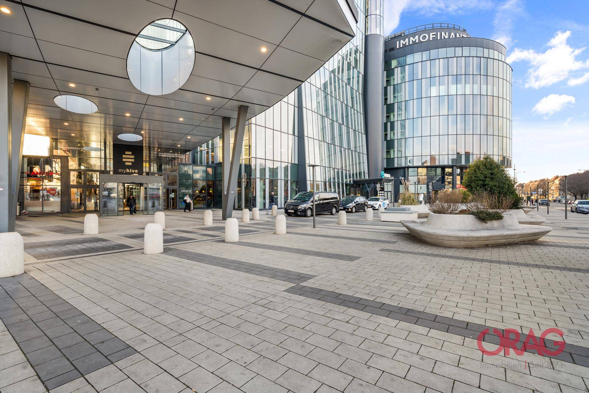Beeindruckende moderne Glasfassade eines Bürogebäudes mit gepflastertem Vorplatz und urbaner Umgebung.