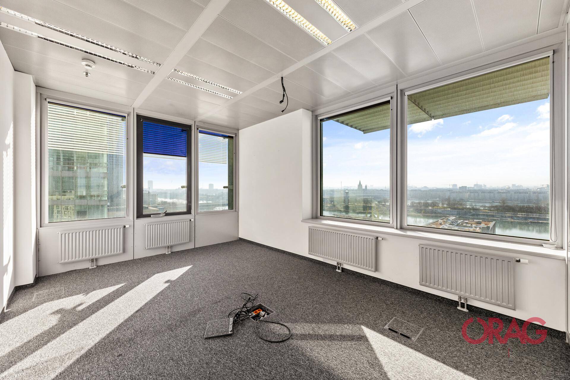 Helles Büro mit Teppichboden, großen Fenstern und weitem Blick auf die Stadt und den Fluss.