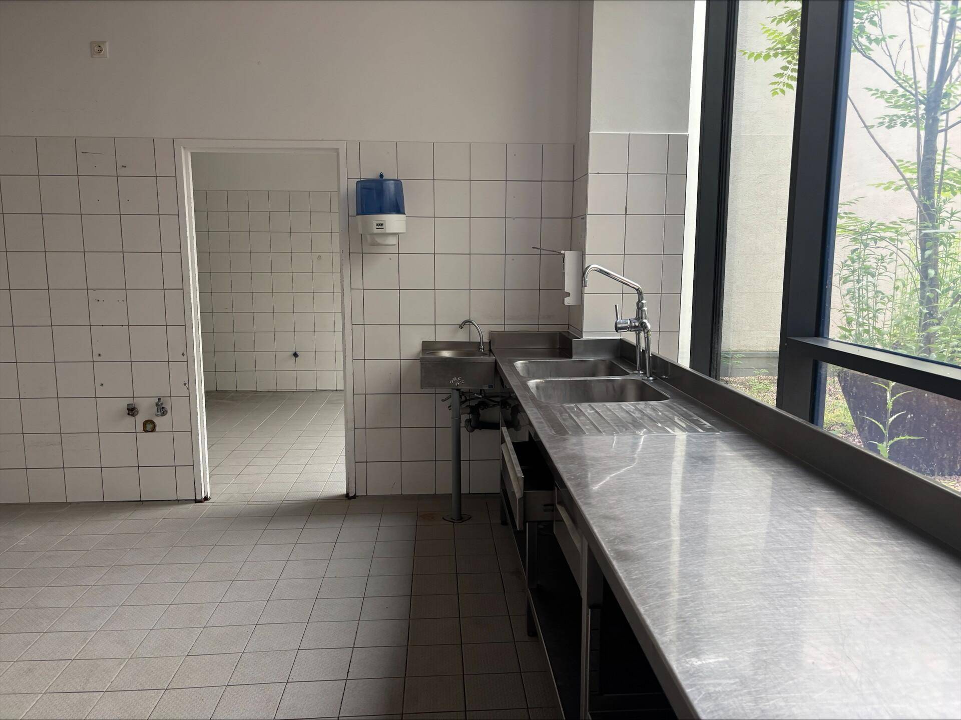 Küchenbereich mit Edelstahlspülbecken, gefliesten Wänden und einem Fenster mit Blick ins Grüne.