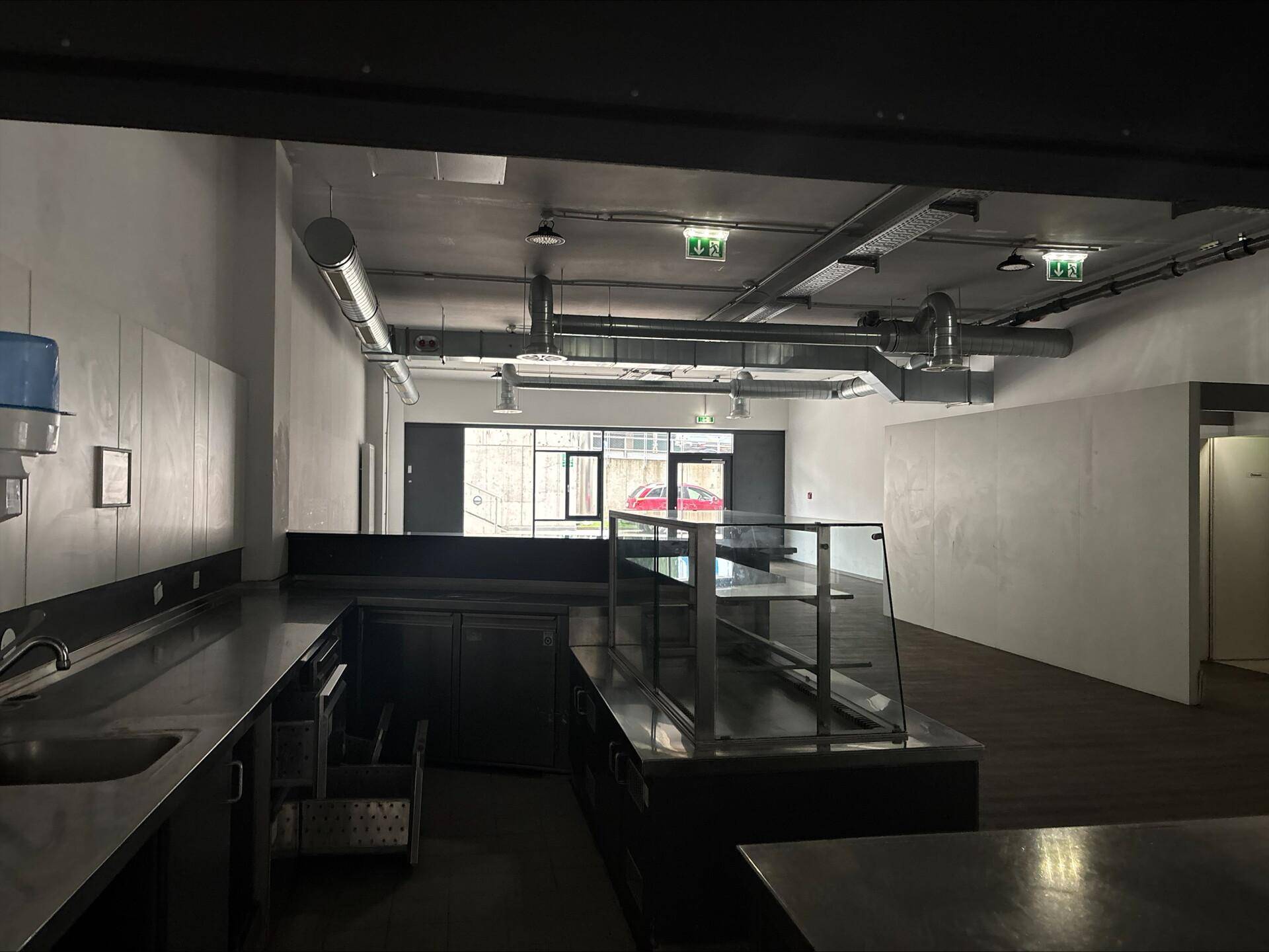Blick von der Küche in den Kantinenbereich mit Theke und großen Fenstern.