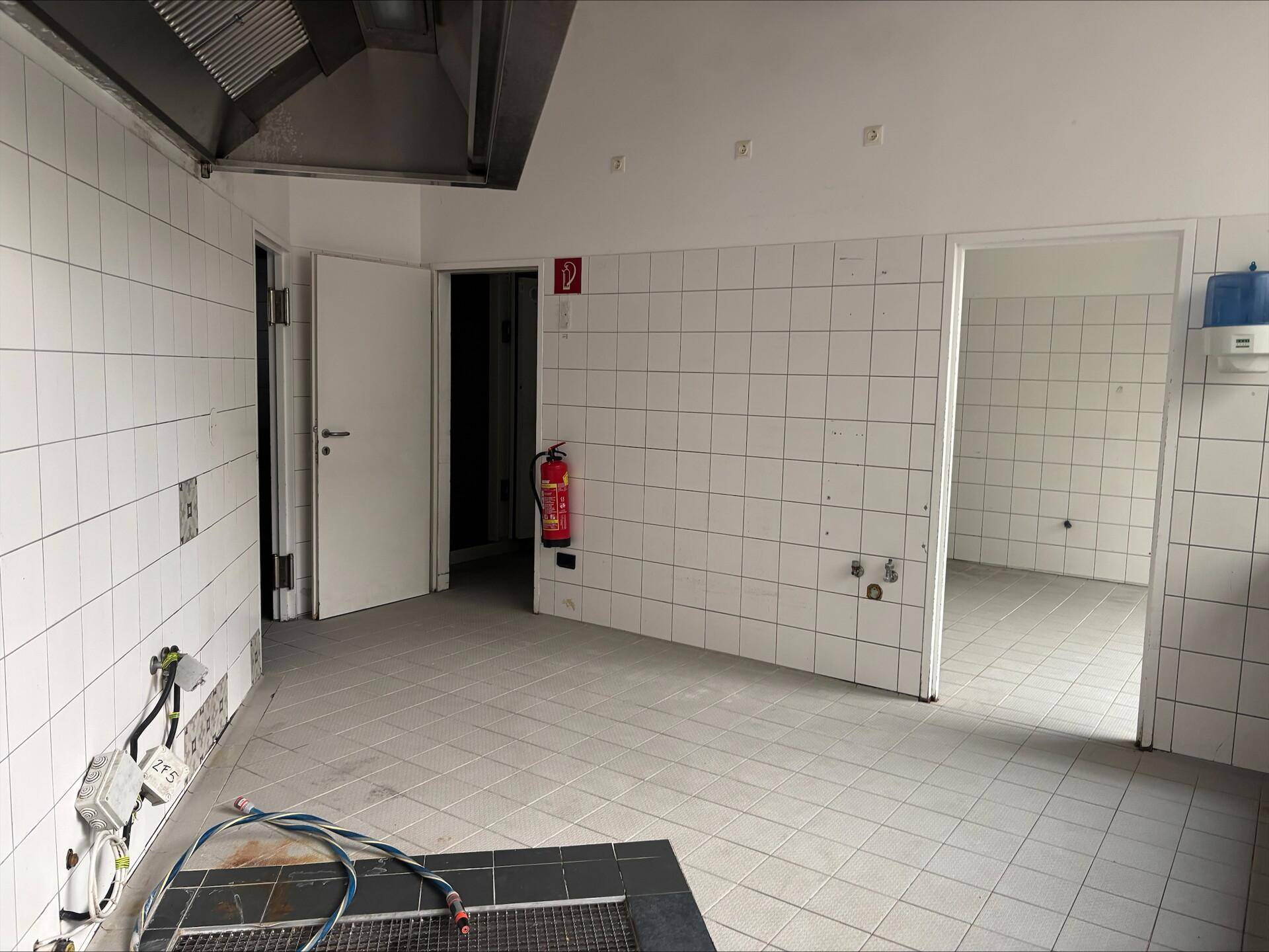 Gefliester Küchenraum mit Türen zu weiteren Bereichen und einem Feuerlöscher an der Wand.