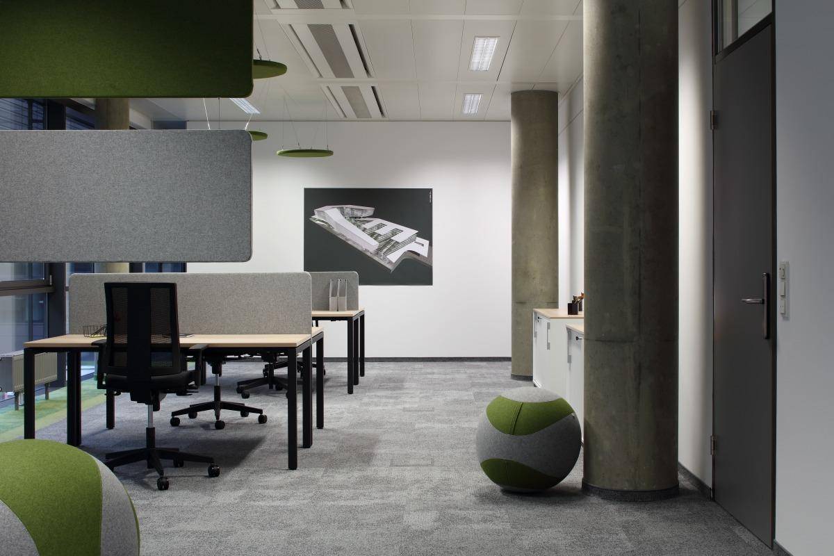 Offener Bürobereich mit modernen Arbeitsplätzen, ergonomischen Stühlen und schallabsorbierenden Elementen.