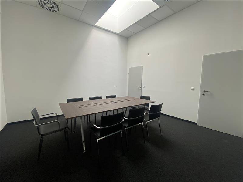 Besprechungsraum mit großem Tisch, Stühlen und dunklem Teppichboden.