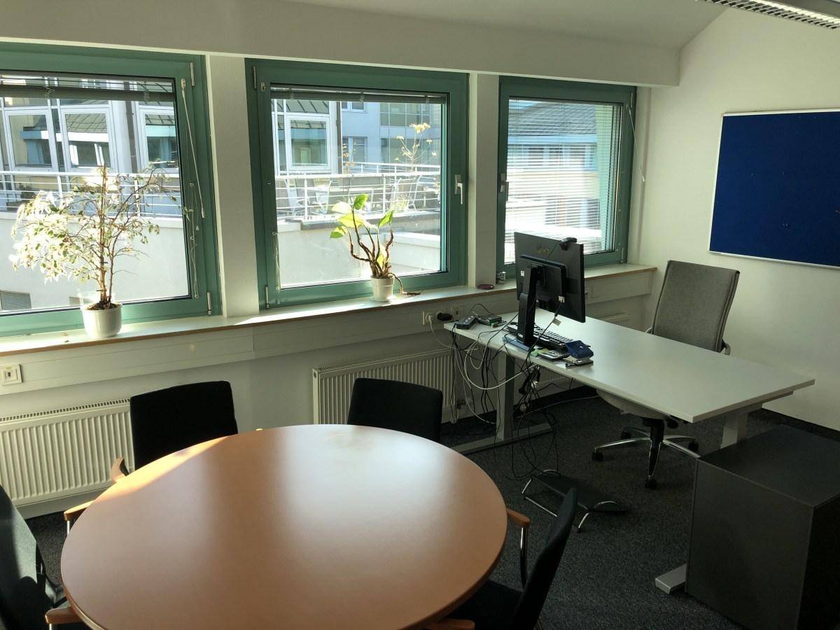 Helles Büro mit großen Fenstern, die viel Tageslicht hereinlassen, und einem runden Besprechungstisch.