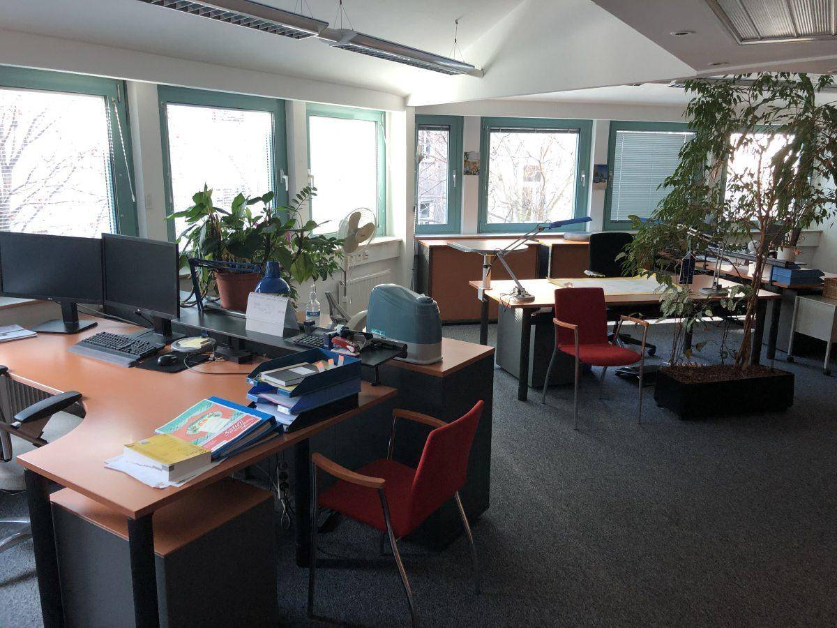Großraumbüro mit mehreren Arbeitsplätzen, großen Fenstern und Pflanzen für eine angenehme Atmosphäre.