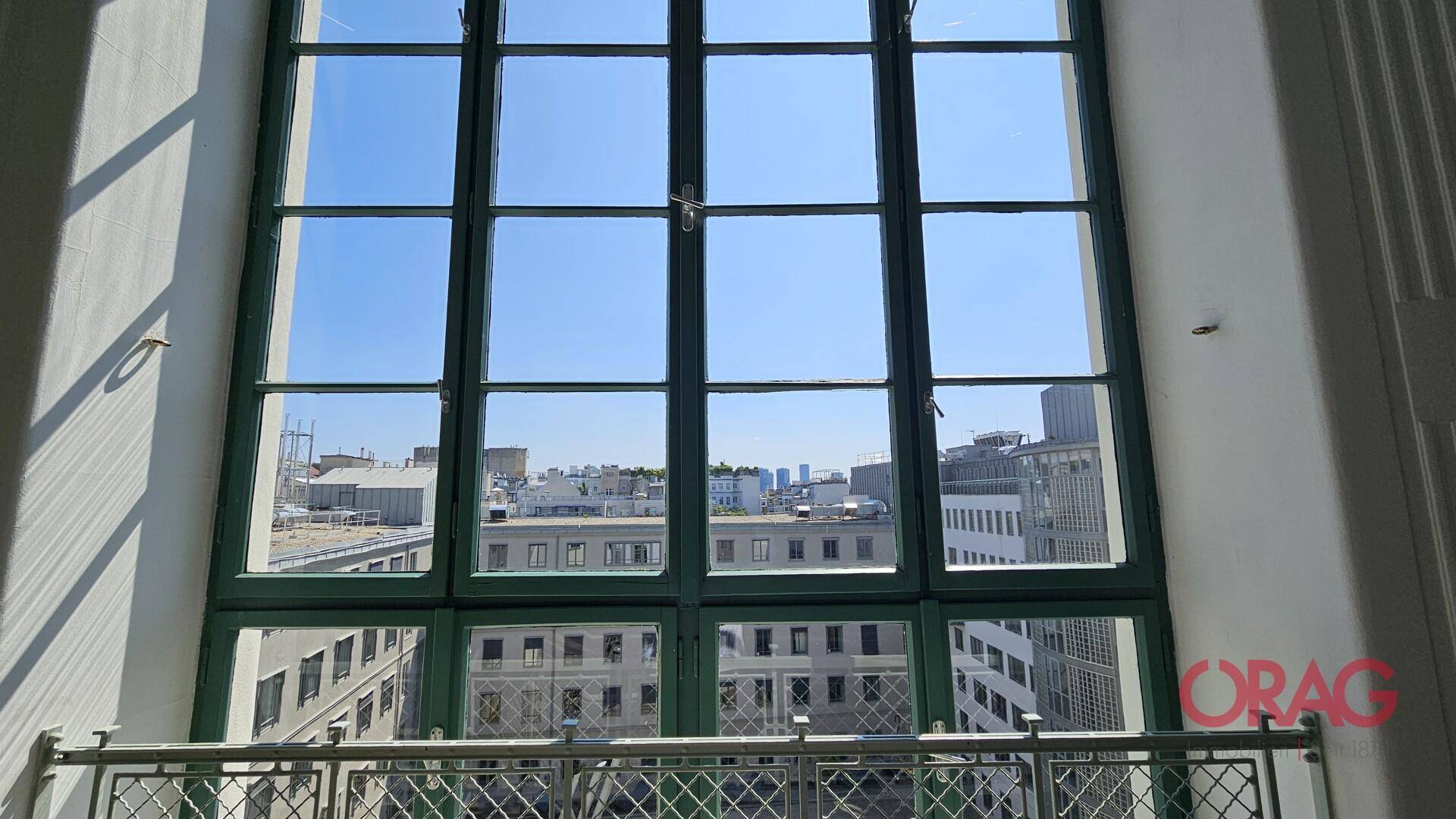 Großes Fenster mit grünen Rahmen bietet einen weiten Blick über die Dächer und die Stadtlandschaft.