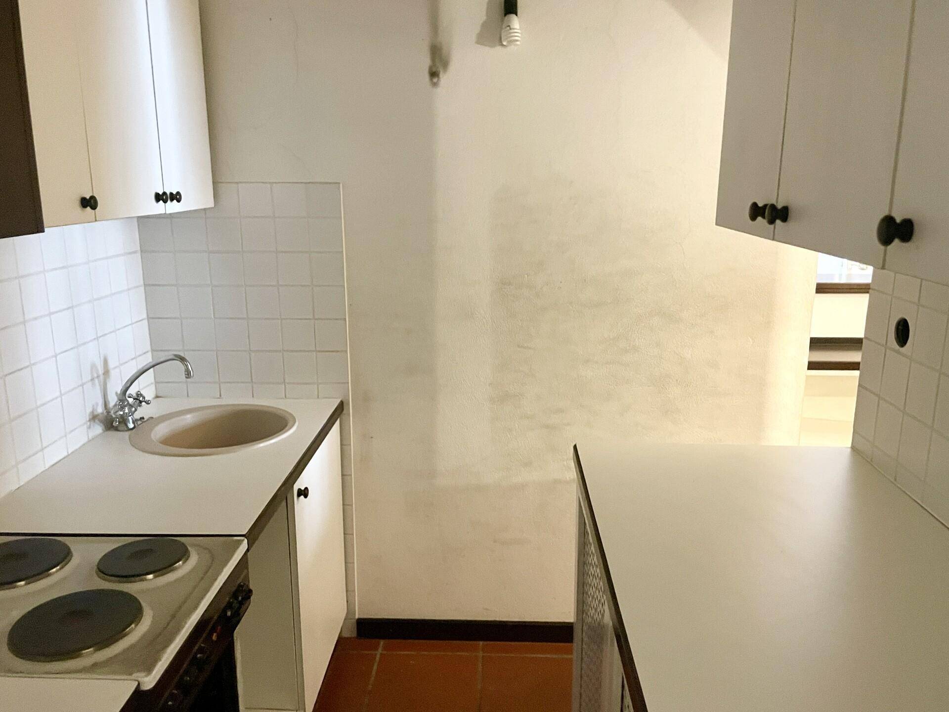 Einfache Küchenzeile mit weißen Schränken, Spüle und Kochfeld, ideal für kleine Räume.