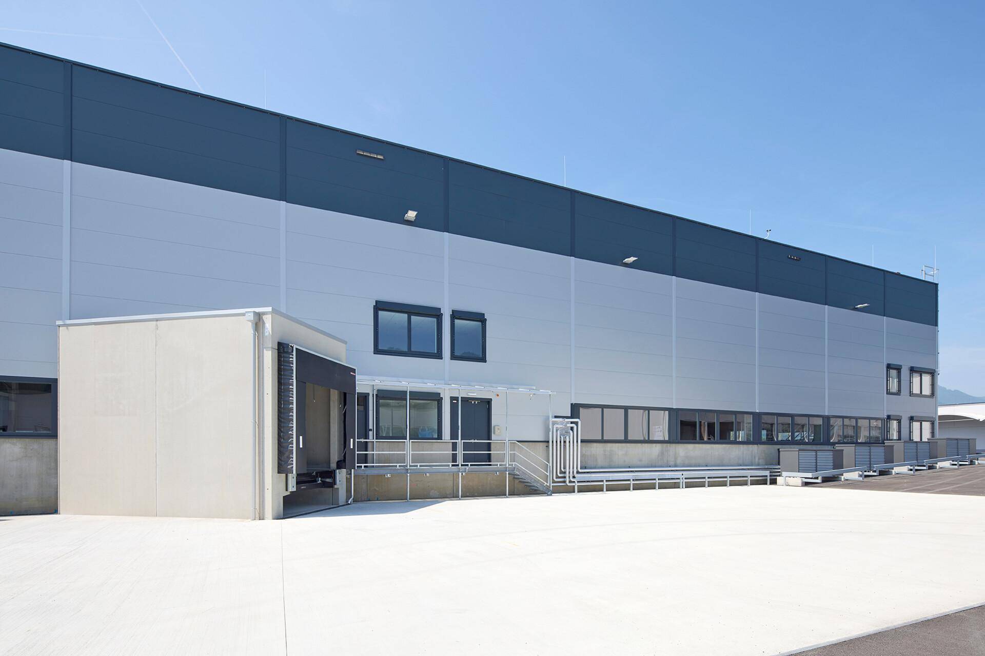 Seitenansicht des modernen Industriegebäudes mit Eingangsbereich, Fenstern und Laderampe.