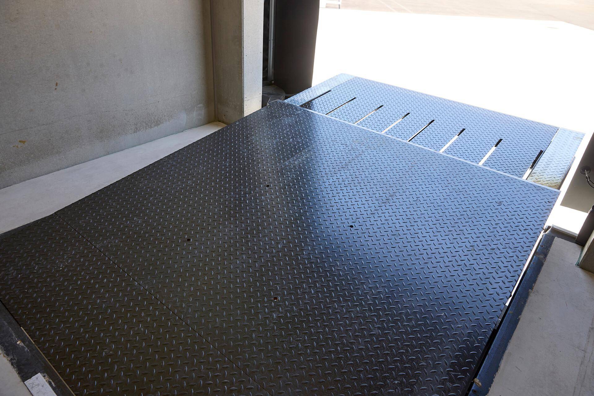 Detailansicht einer robusten Metall-Laderampe mit rutschfester Riffelblech-Oberfläche für den Warenverkehr.