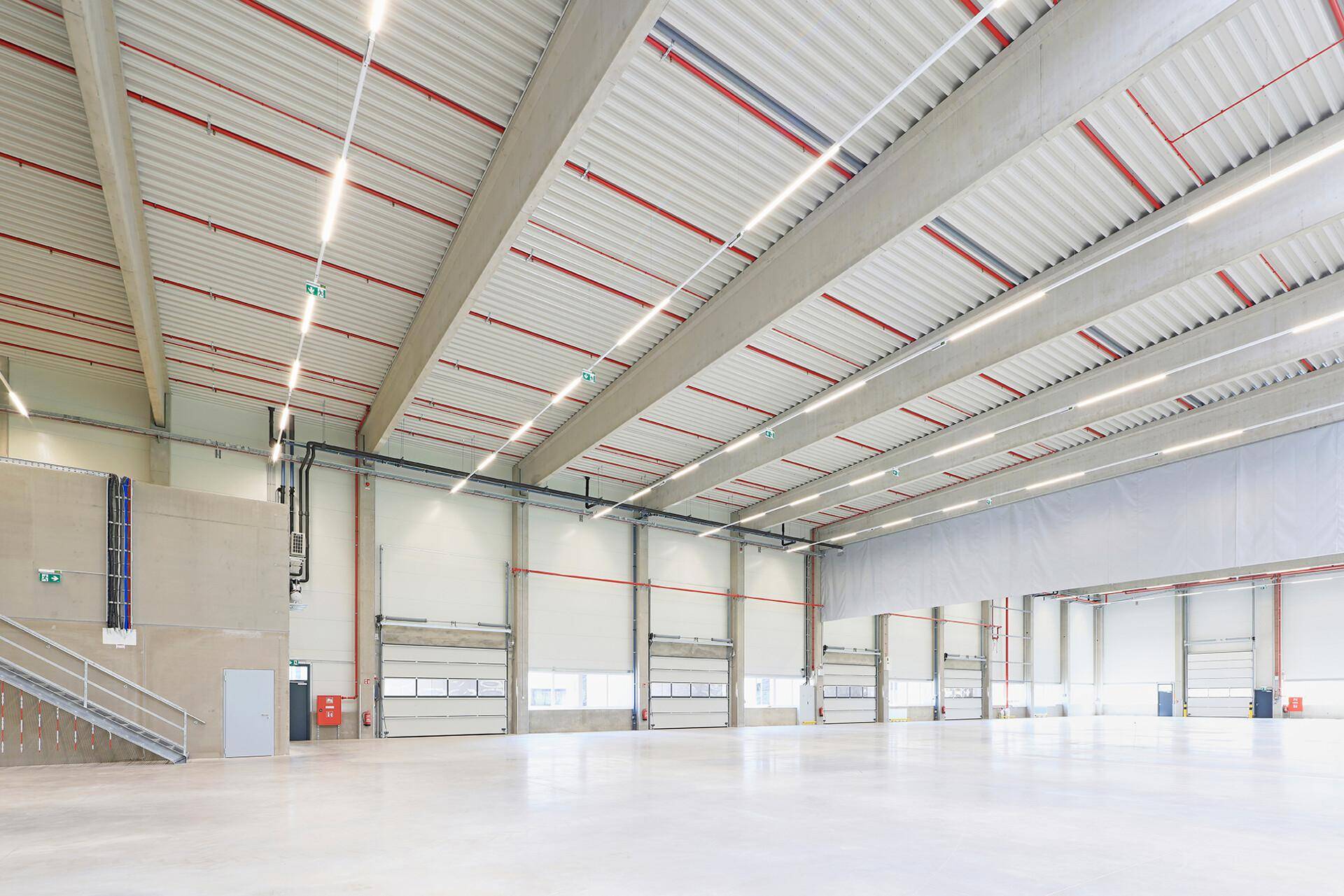 Weitläufige Lagerhalle mit mehreren Rolltoren, einer Treppe und heller Beleuchtung.