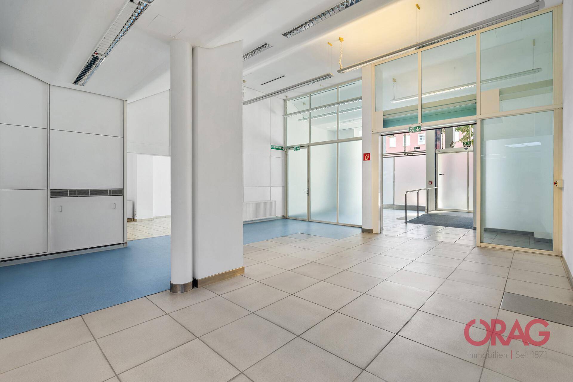 Heller Gewerberaum mit Fliesenboden, Glasabtrennungen und Eingangsbereich, vielseitig nutzbar.