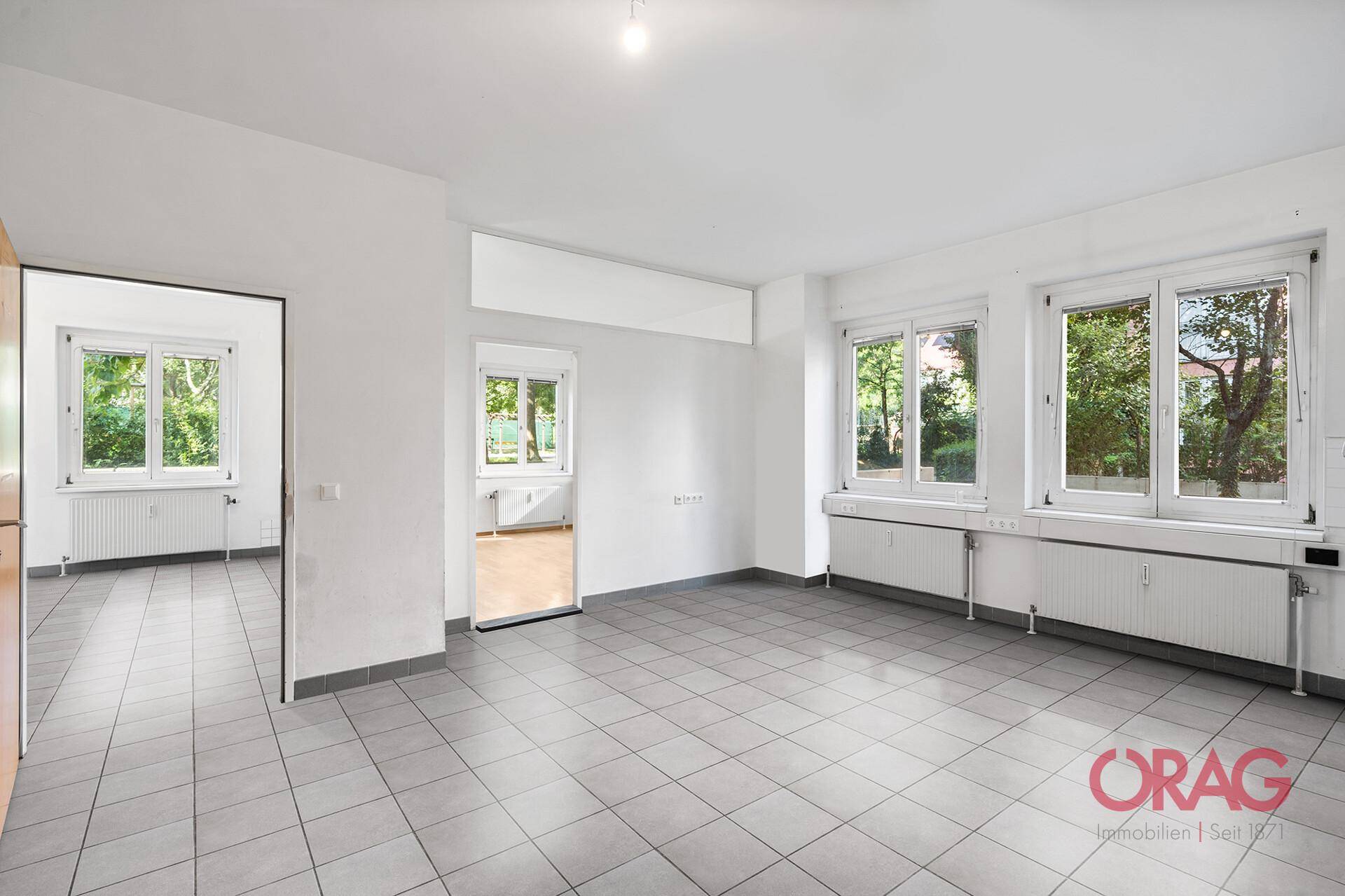 Heller, leerer Raum mit Fliesenboden und großen Fenstern, die viel Tageslicht hereinlassen.