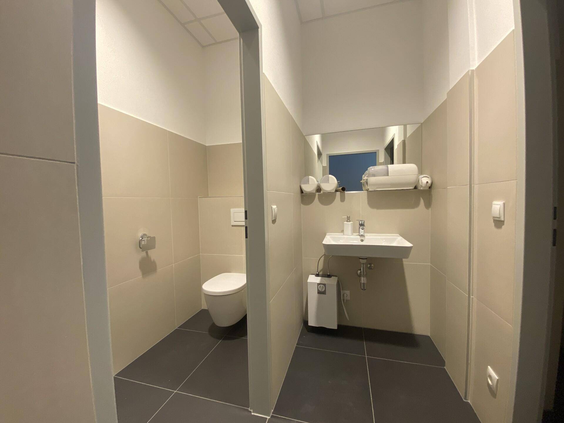 Modernes WC mit wandhängender Toilette, Waschbecken und stilvollen Fliesen in Beige und Grau.