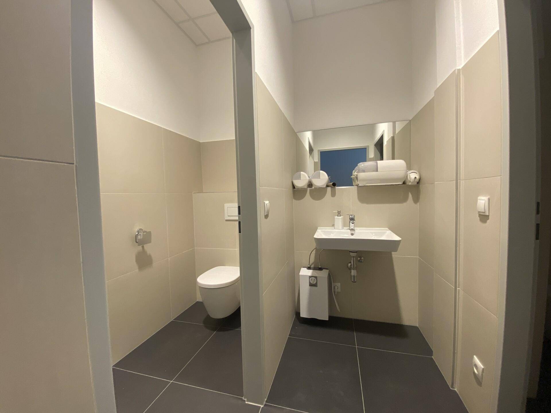 Saubere Toilette mit wandhängendem WC, Waschbecken und Spiegel, gefliest in Beige und Grau.