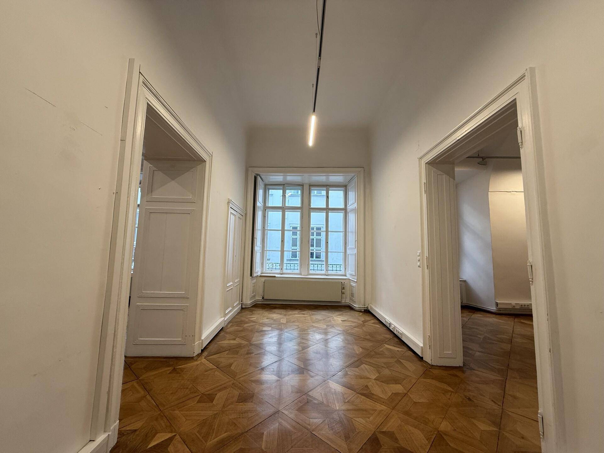 Heller Flur mit elegantem Parkettboden, großem Fenster und Zugang zu angrenzenden Räumen.