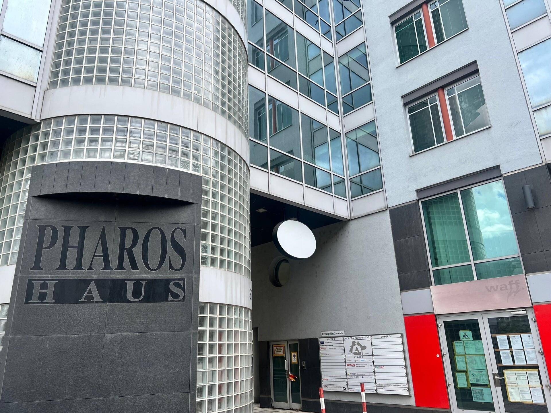 Eingangsbereich des "PHAROS HAUS" mit moderner Fassade, Glasbausteinen und einem markanten Schriftzug.