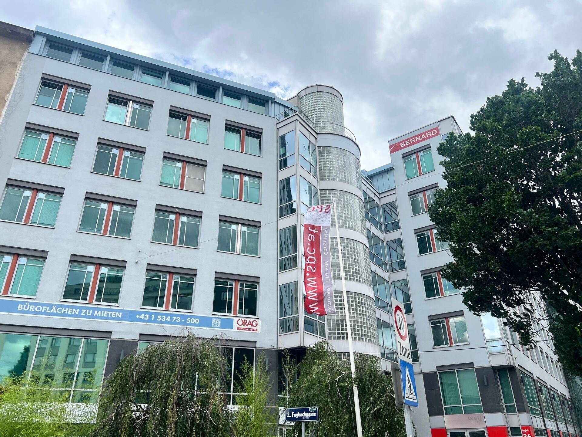 Außenansicht eines modernen Bürogebäudes mit vielen Fenstern und einem Werbebanner für Mietflächen.