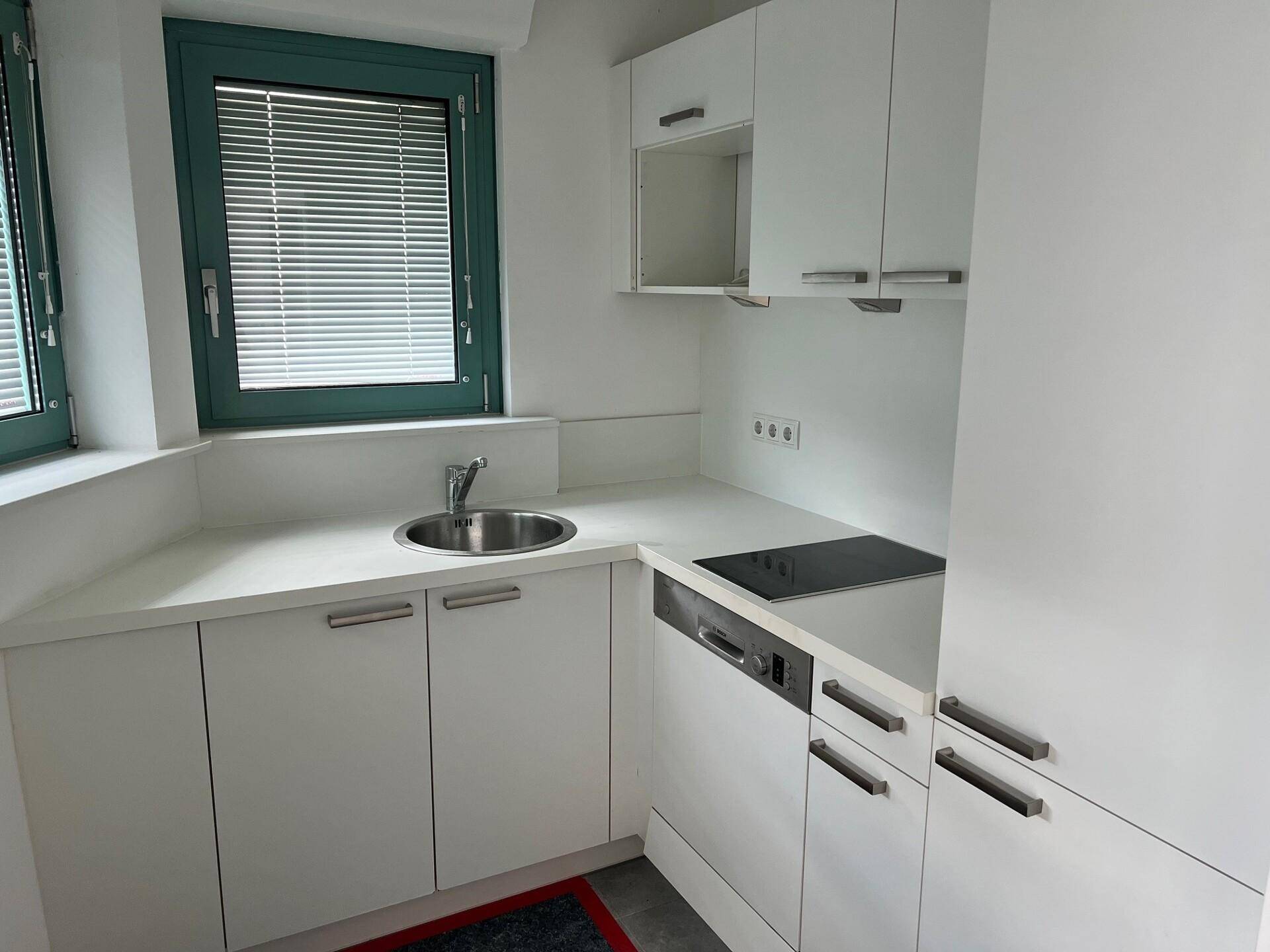 Moderne Küchenzeile mit weißen Schränken, Spüle, Induktionskochfeld und einem Fenster mit Jalousien.