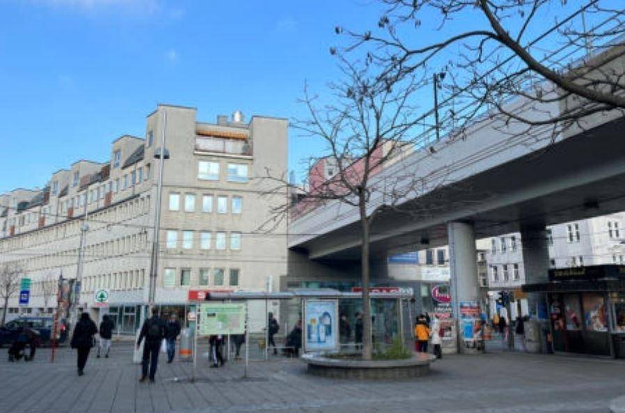 Eine belebte Stadtstraße mit Fußgängern, Gebäuden und einer erhöhten U-Bahn-Linie.