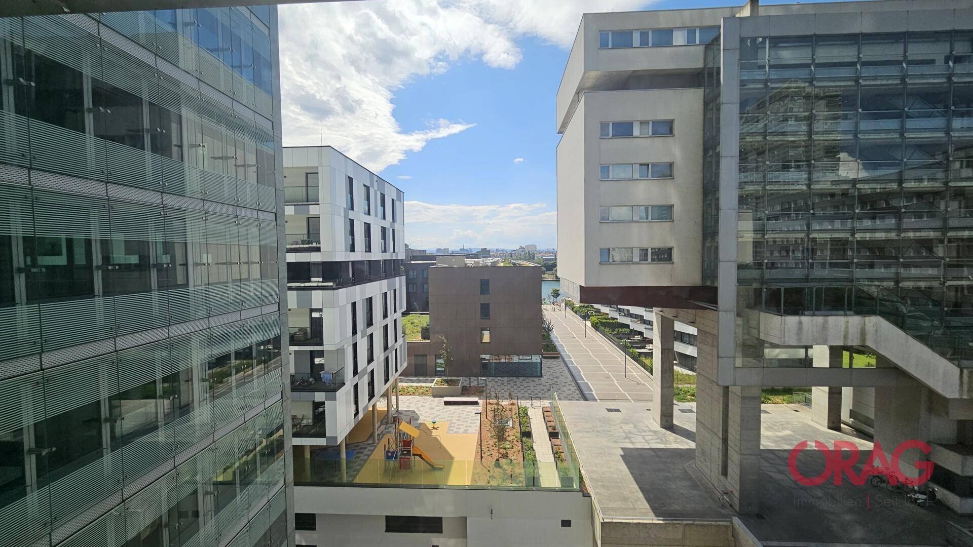 Blick aus dem Fenster auf moderne Gebäude, einen Spielplatz und den Himmel.