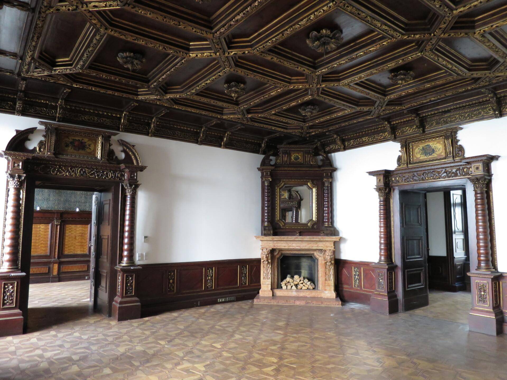 Prunkvoller Raum mit dunkler Holzvertäfelung, Kassettendecke, Kamin und elegantem Parkettboden.