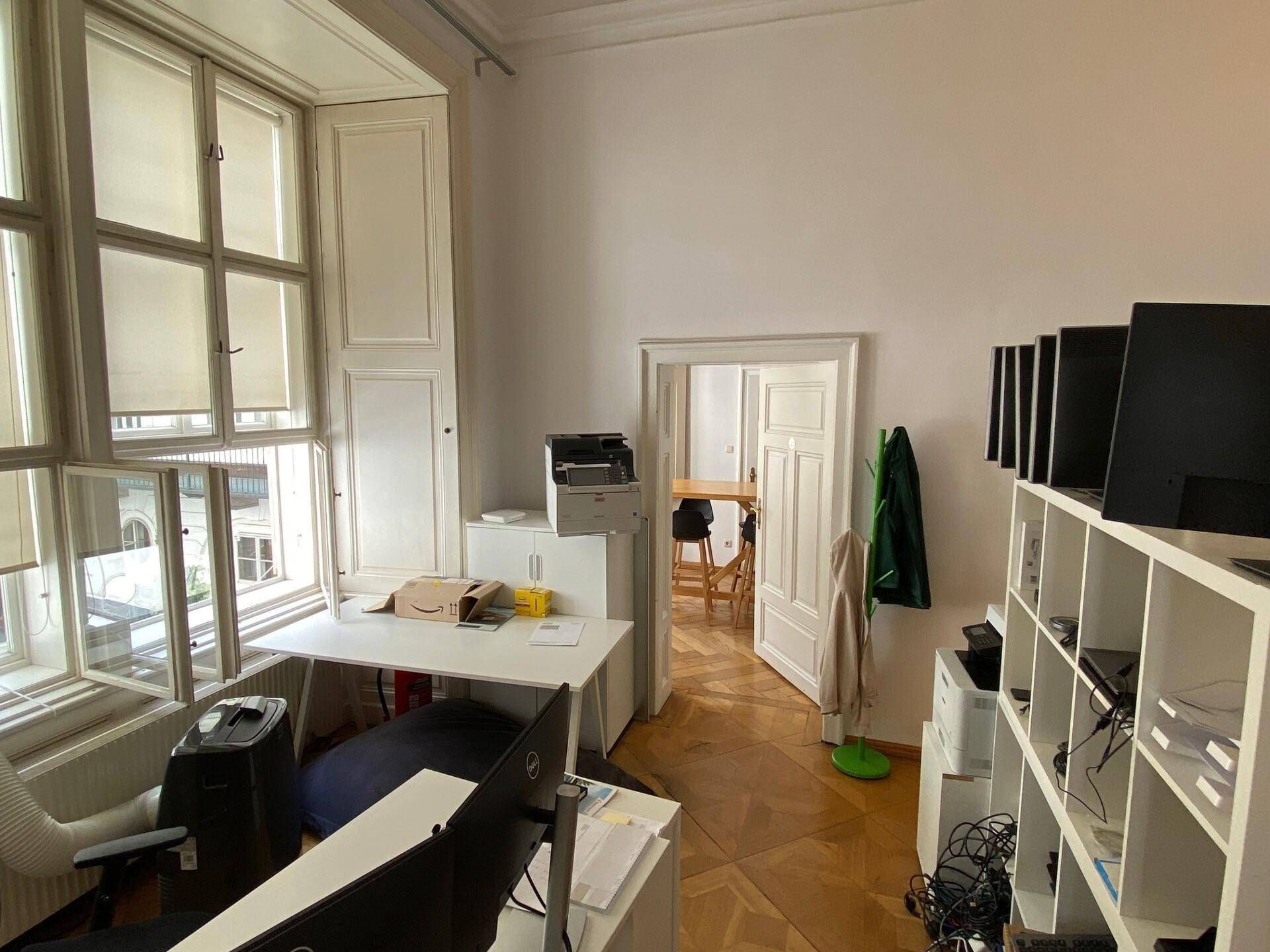 Büroarbeitsplatz mit Schreibtisch, Computermonitoren, Regalen und großen Fenstern, die viel Tageslicht bieten.