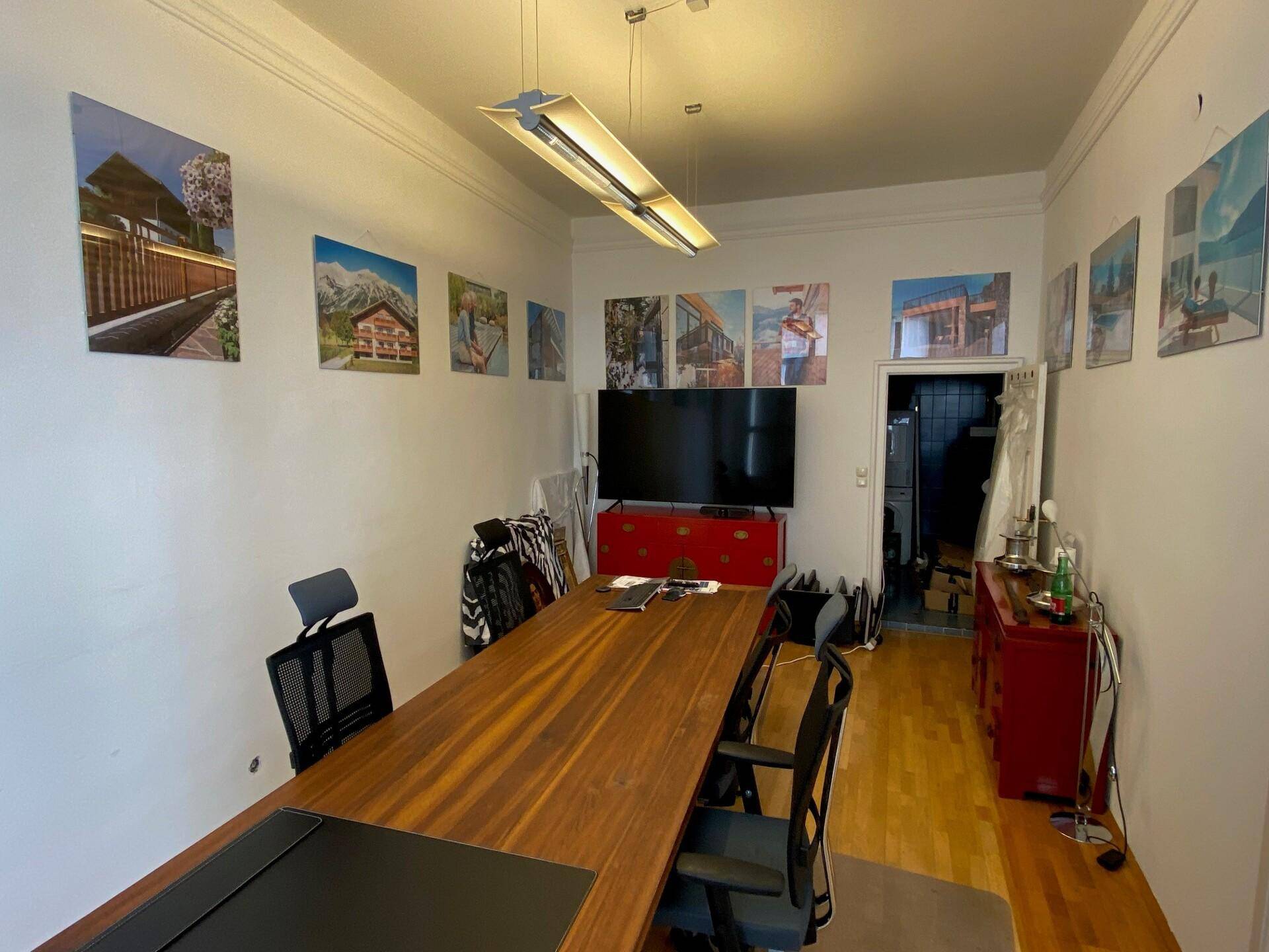 Besprechungsraum mit einem langen Holztisch, Stühlen, einem großen Fernseher und Bildern an der Wand.