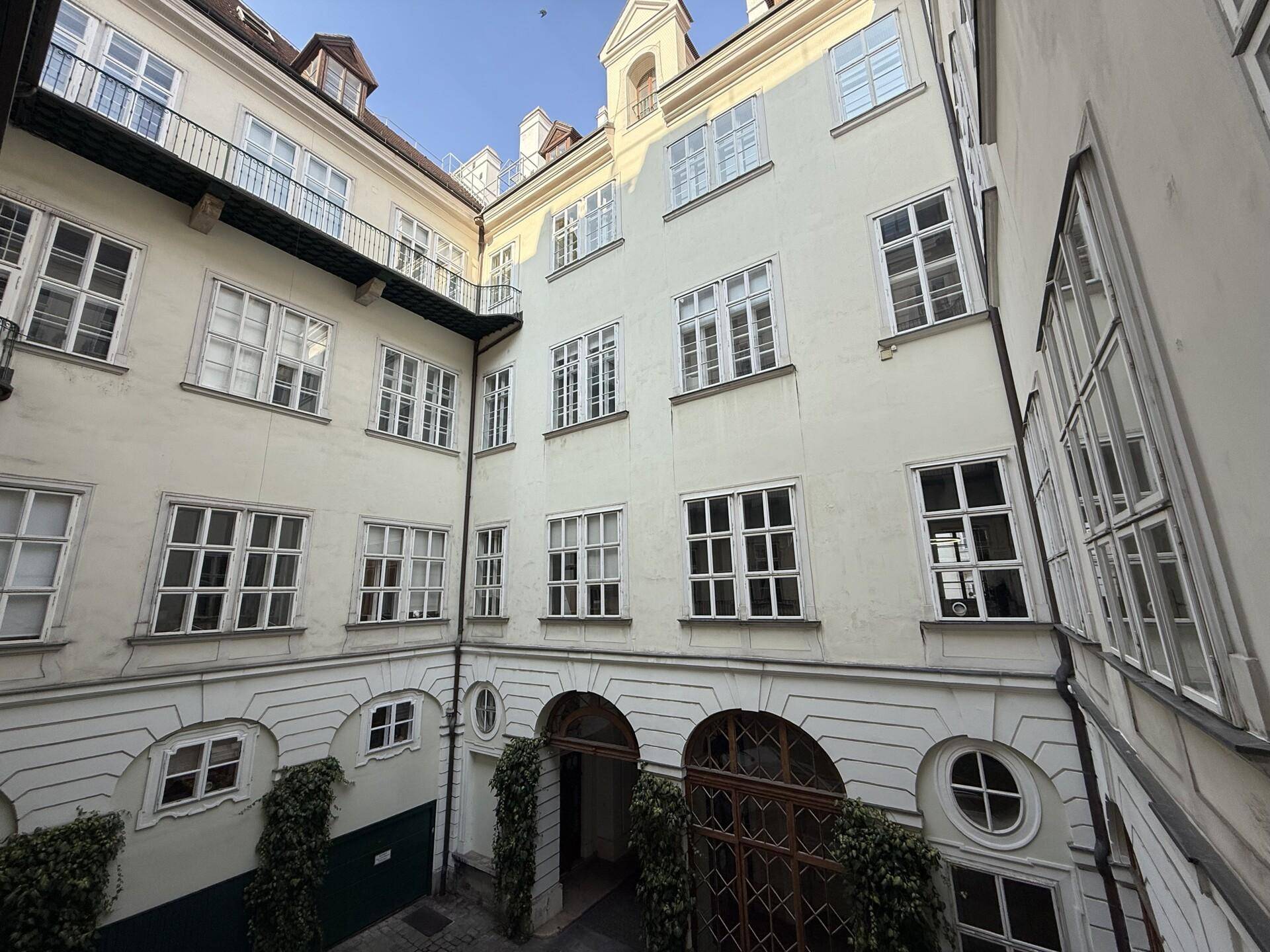 Innenhof eines historischen Gebäudes mit vielen Fenstern und Efeu an den Wänden.