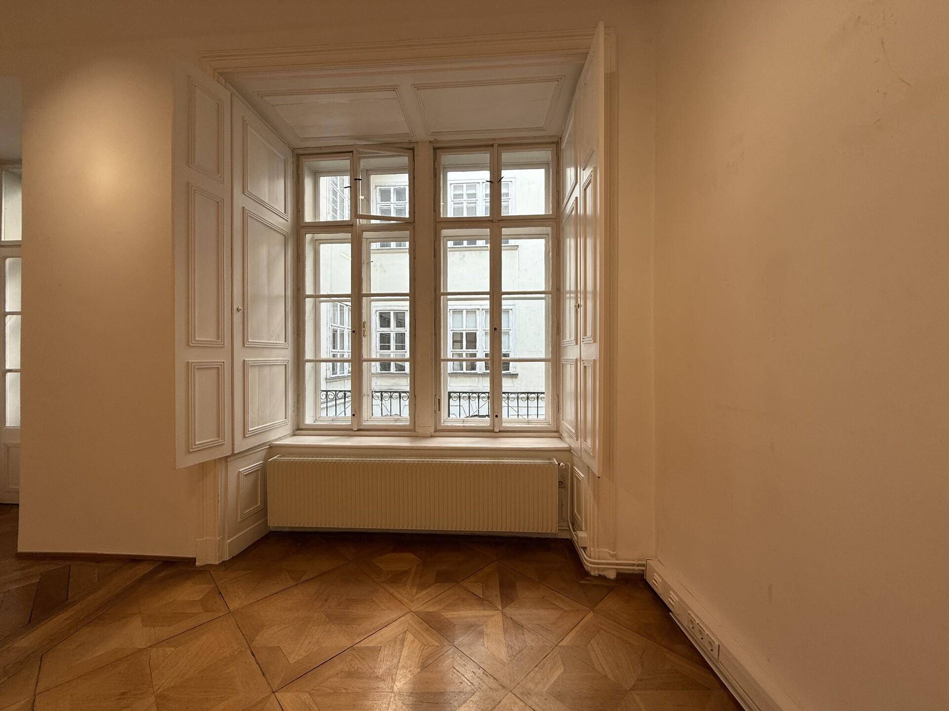 Detailansicht eines großen Fensters mit geöffneten Holzläden und einem Heizkörper in einem hellen Raum.