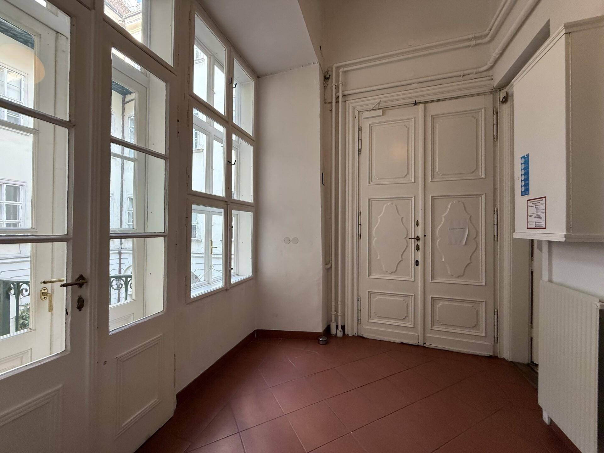 Geschlossene Loggia mit Terrakottafliesen, großen Fenstern und alten Doppeltüren, die viel Licht hereinlassen.