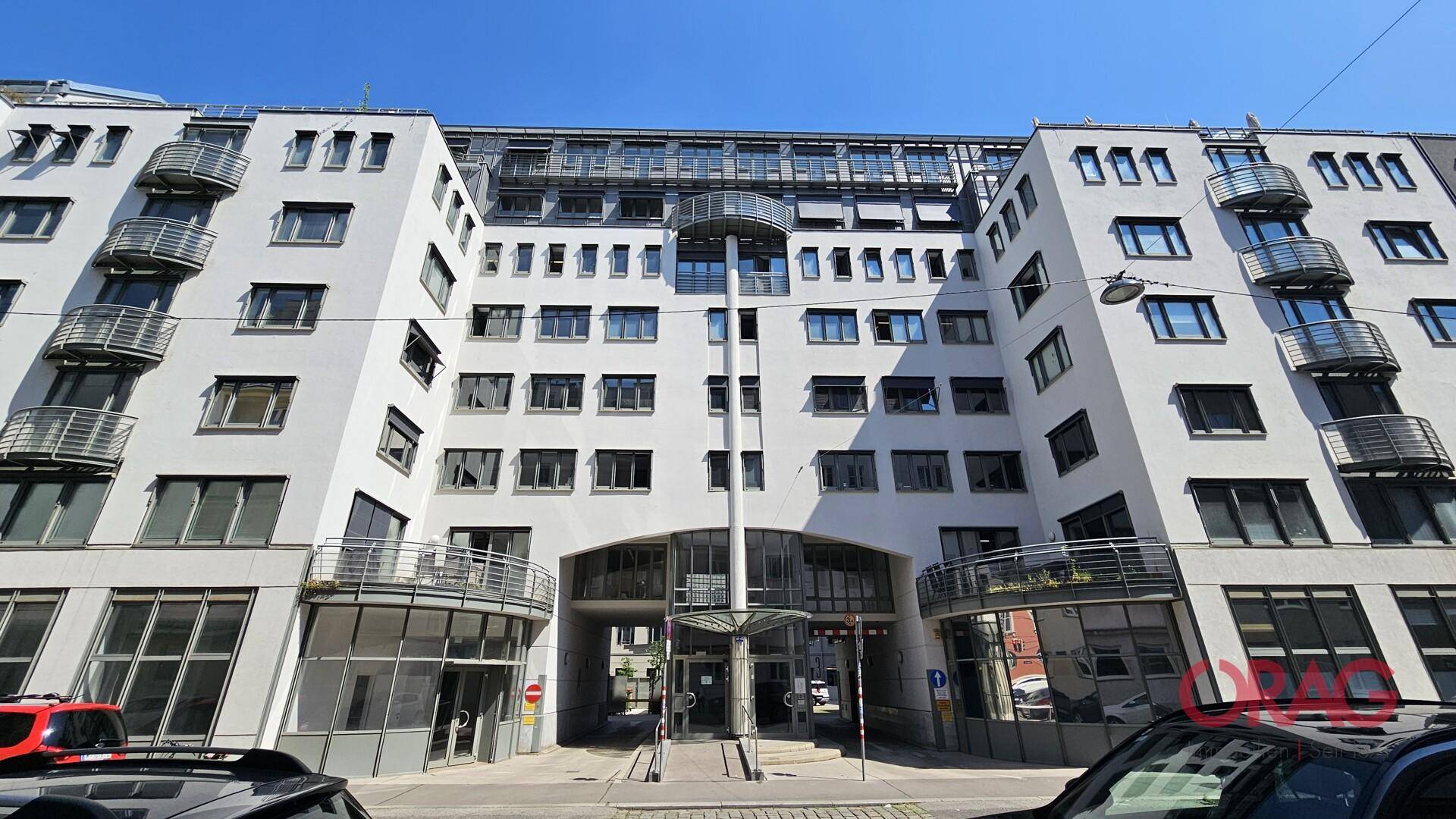 Modernes Bürogebäude mit weißer Fassade, vielen Fenstern und Balkonen unter blauem Himmel.