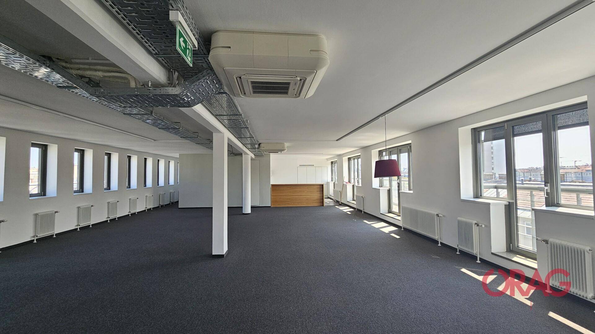 Großzügiger, offener Bürobereich mit Teppichboden, vielen Fenstern und Klimaanlage an der Decke.