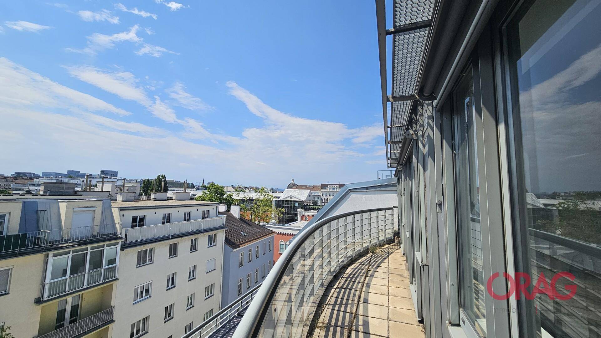 Langer, geschwungener Balkon mit Stadtblick und Metallgeländer unter blauem Himmel.