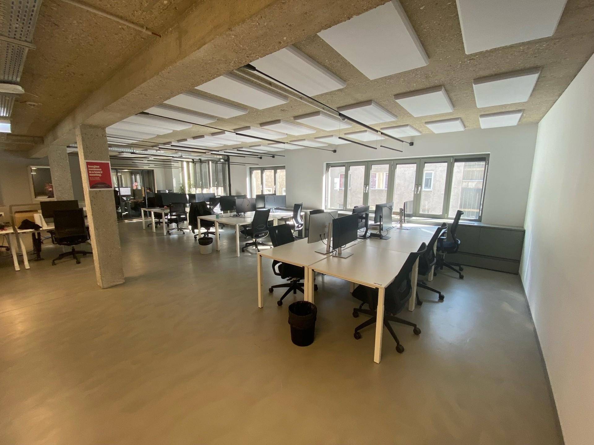 Moderner Großraumbüro mit Schreibtischen, Bürostühlen und schallabsorbierenden Deckenplatten.