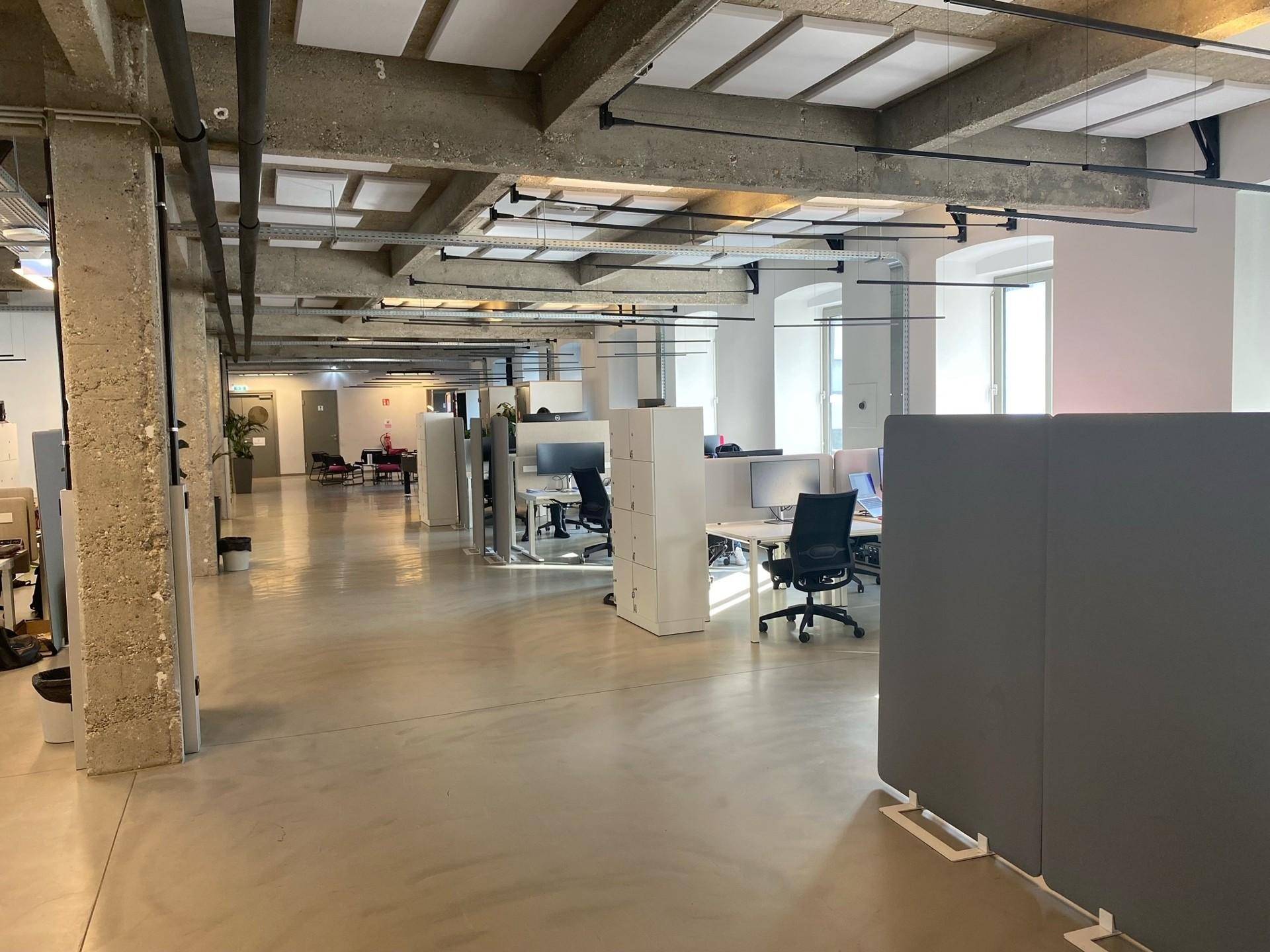 Großraumbüro mit Arbeitsplätzen, Trennwänden und sichtbaren Betonsäulen im modernen Design.