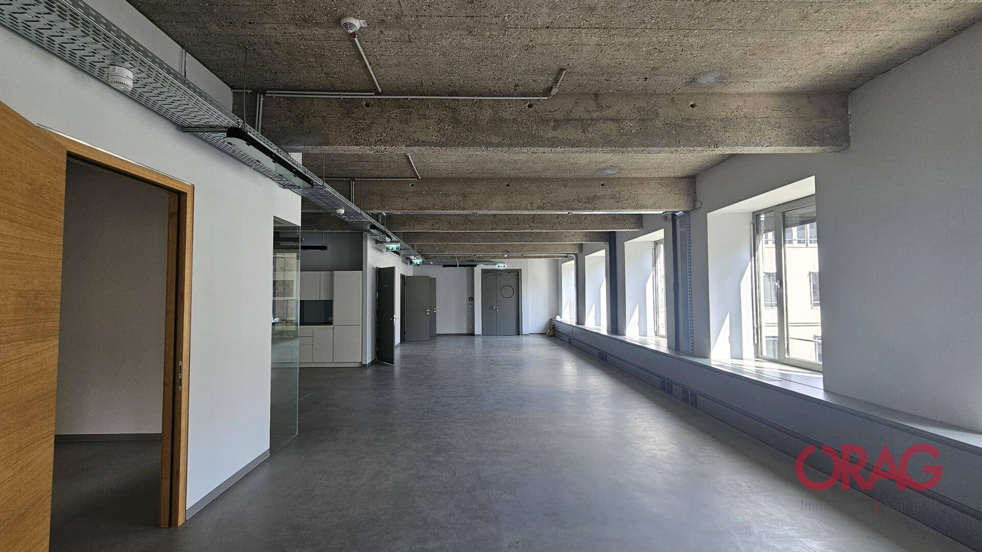 Geräumiger Büroraum mit Sichtbetondecke, großen Fenstern und einem modernen Betonboden.