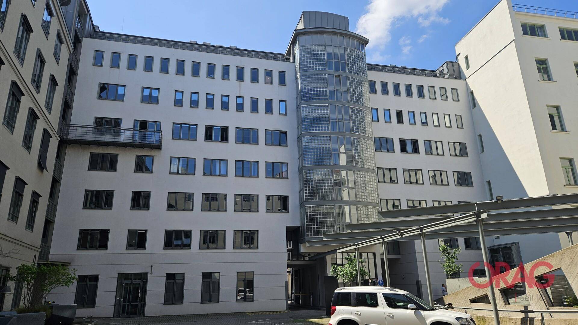 Modernes Bürogebäude mit weißer Fassade und markantem Glaszylinder-Treppenhaus.